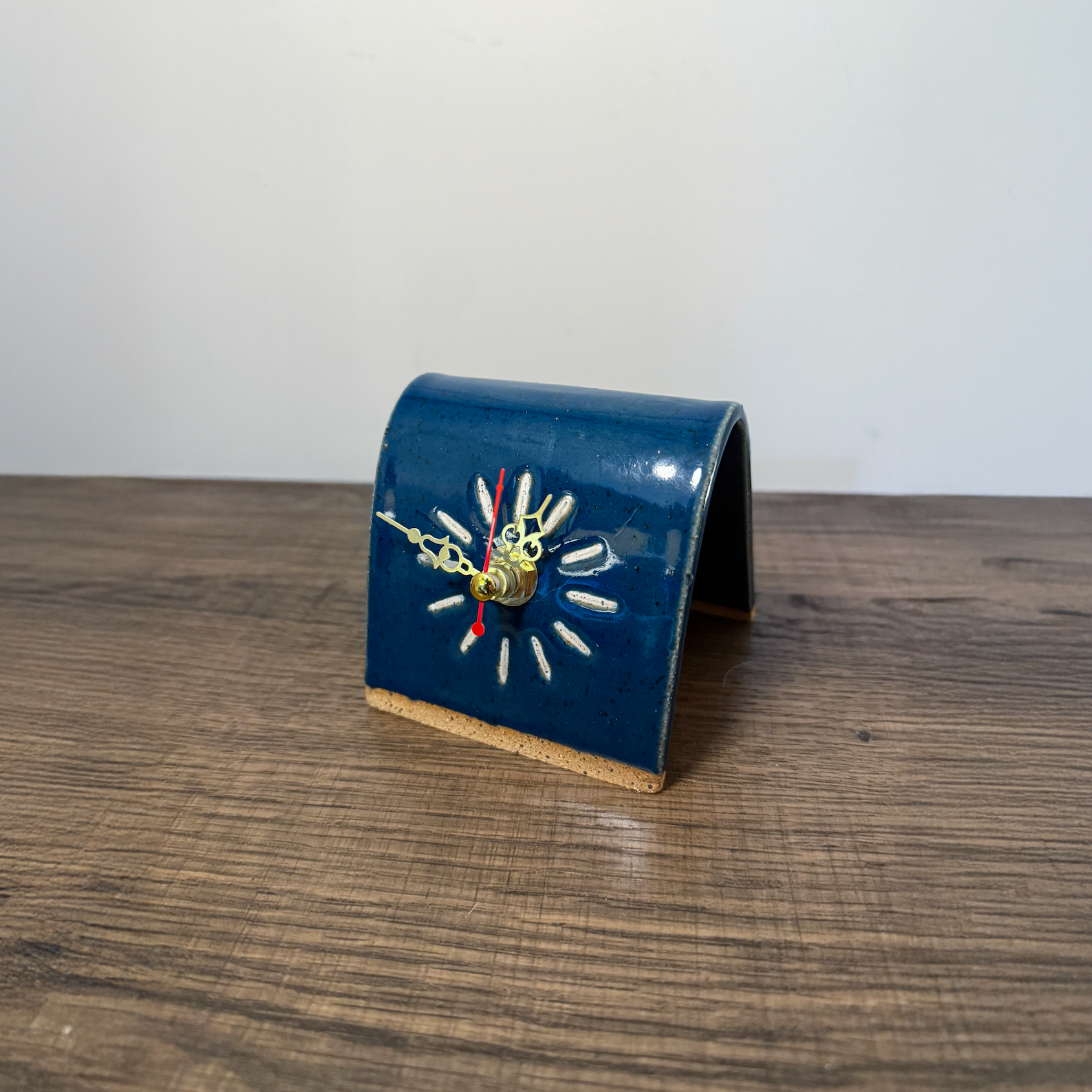 Blue ceramic desk clock on a wooden surface with a white wall background