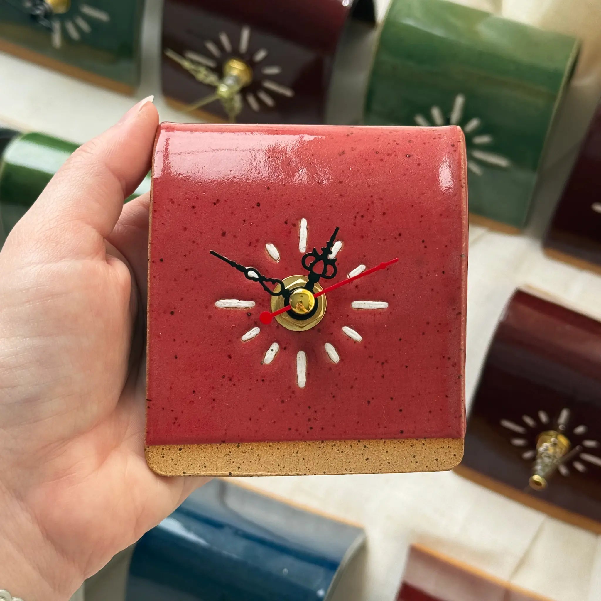 Hand holding a small red clock with a sun design in the center, surrounded by similar clocks.