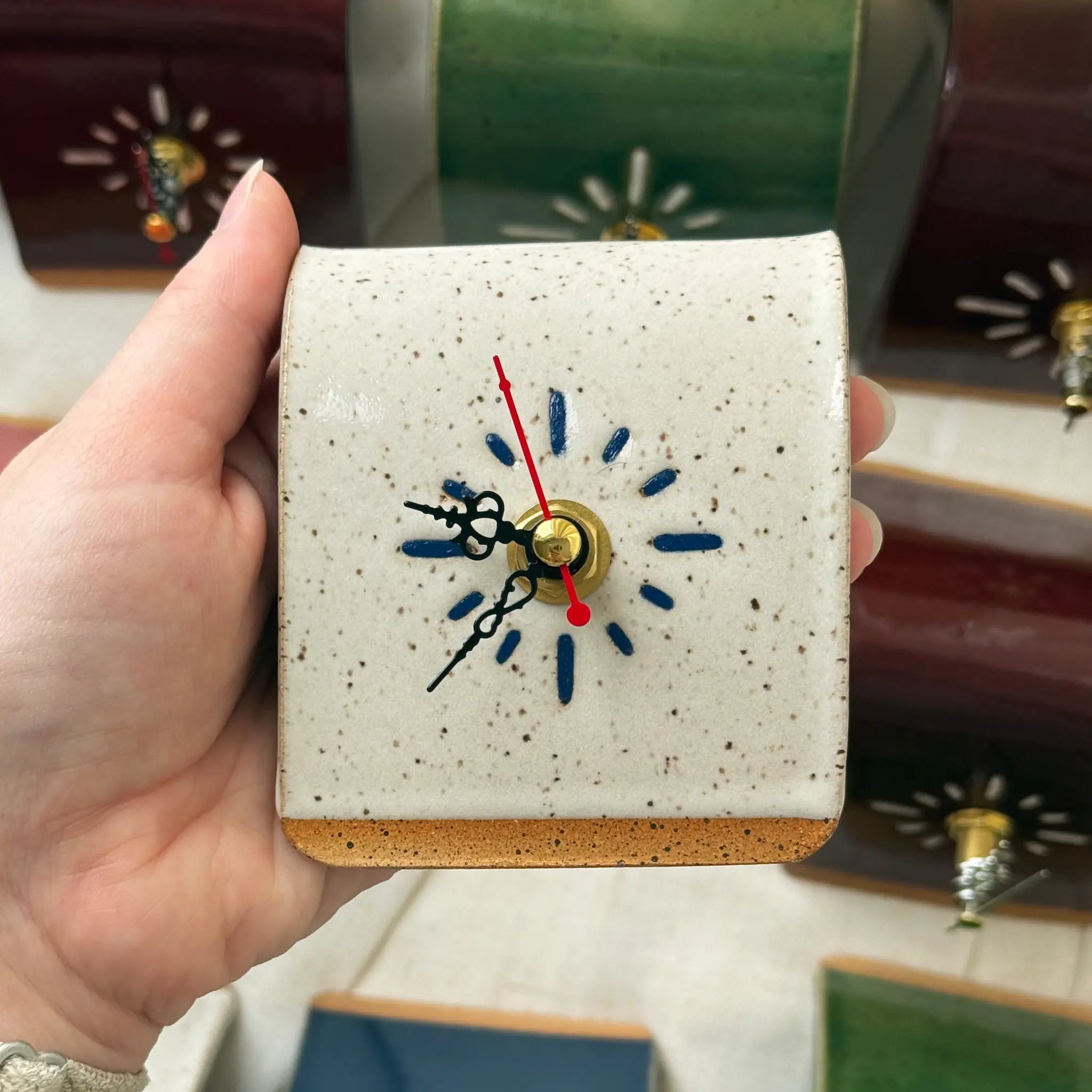 Hand holding a small square clock with speckled design