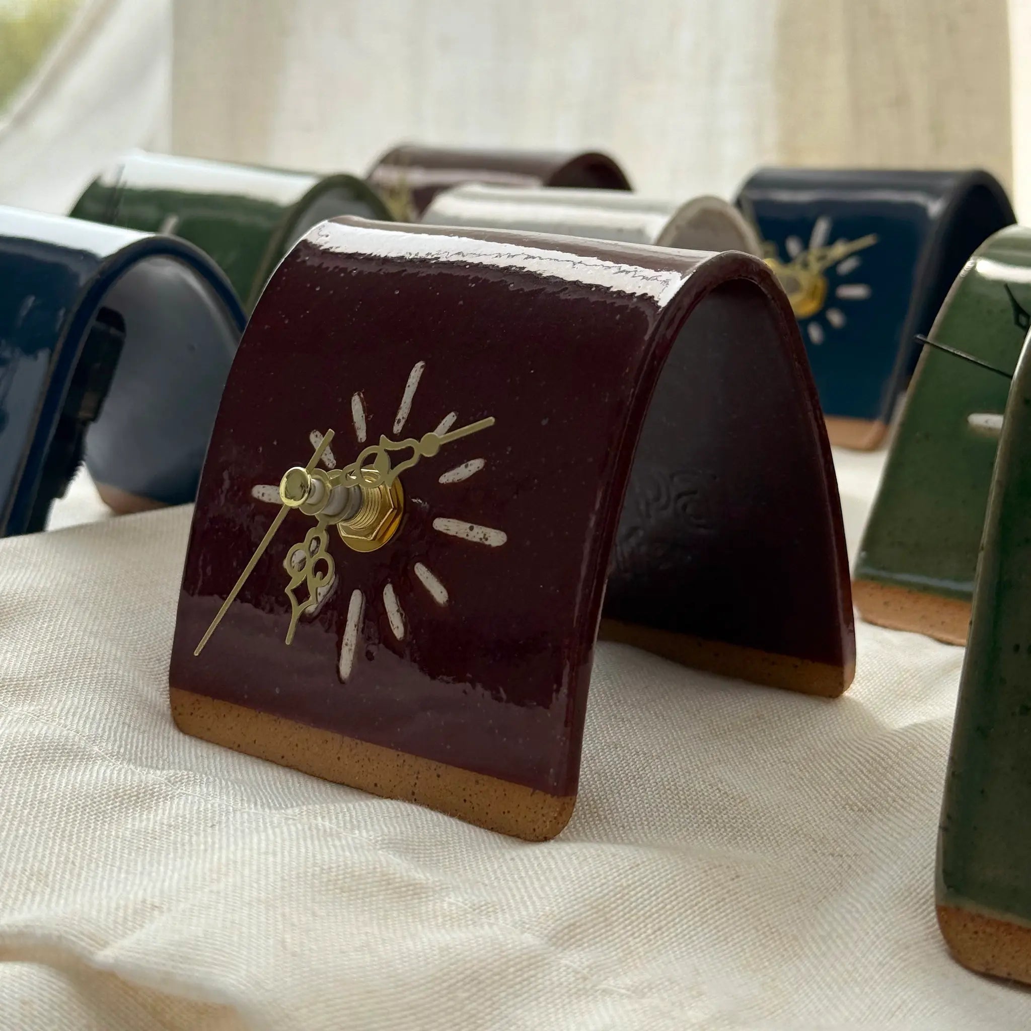 Small ceramic clock with a cordovan body and gold hands on a white fabric background
