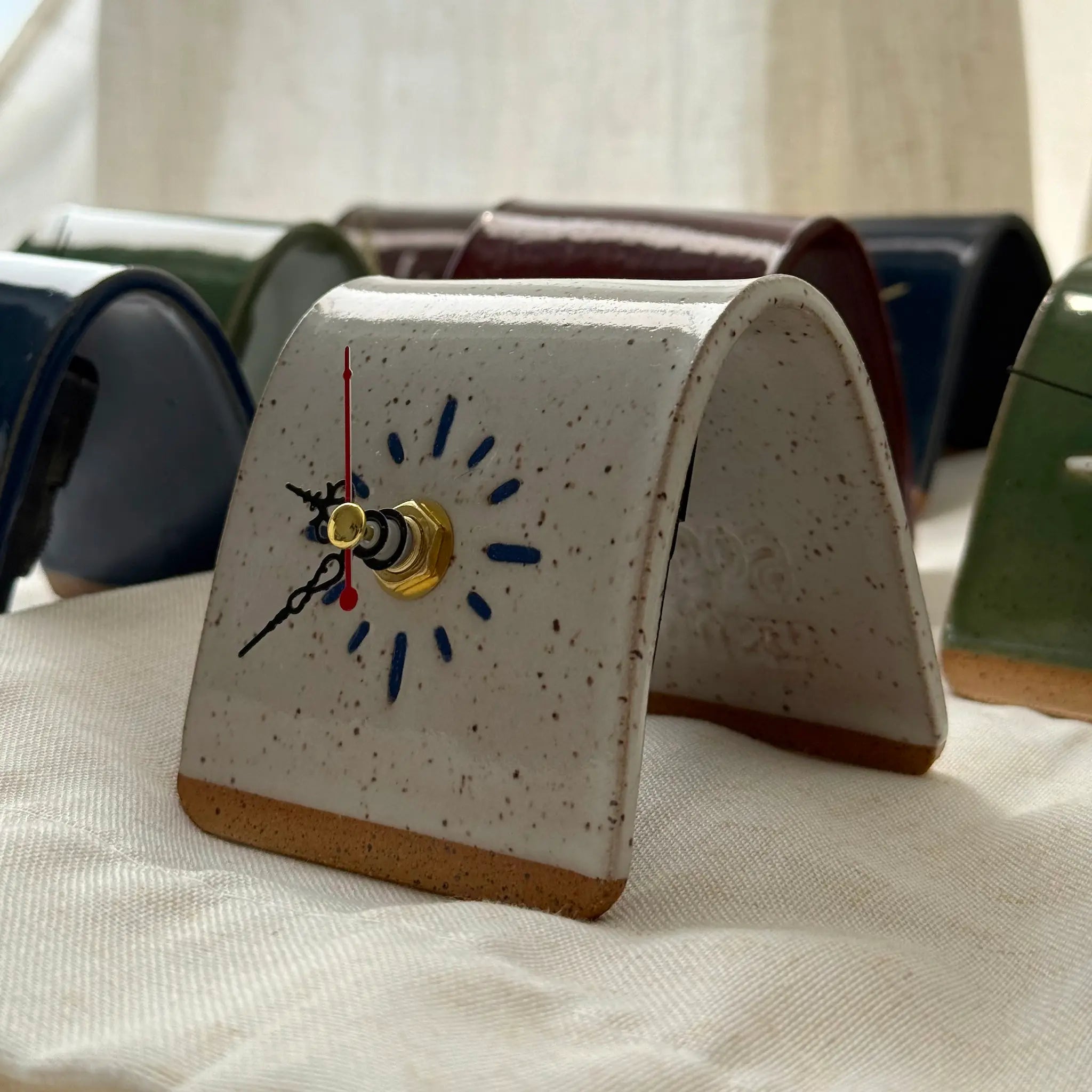 Speckled handmade ceramic clock on a textured surface with blurred background.