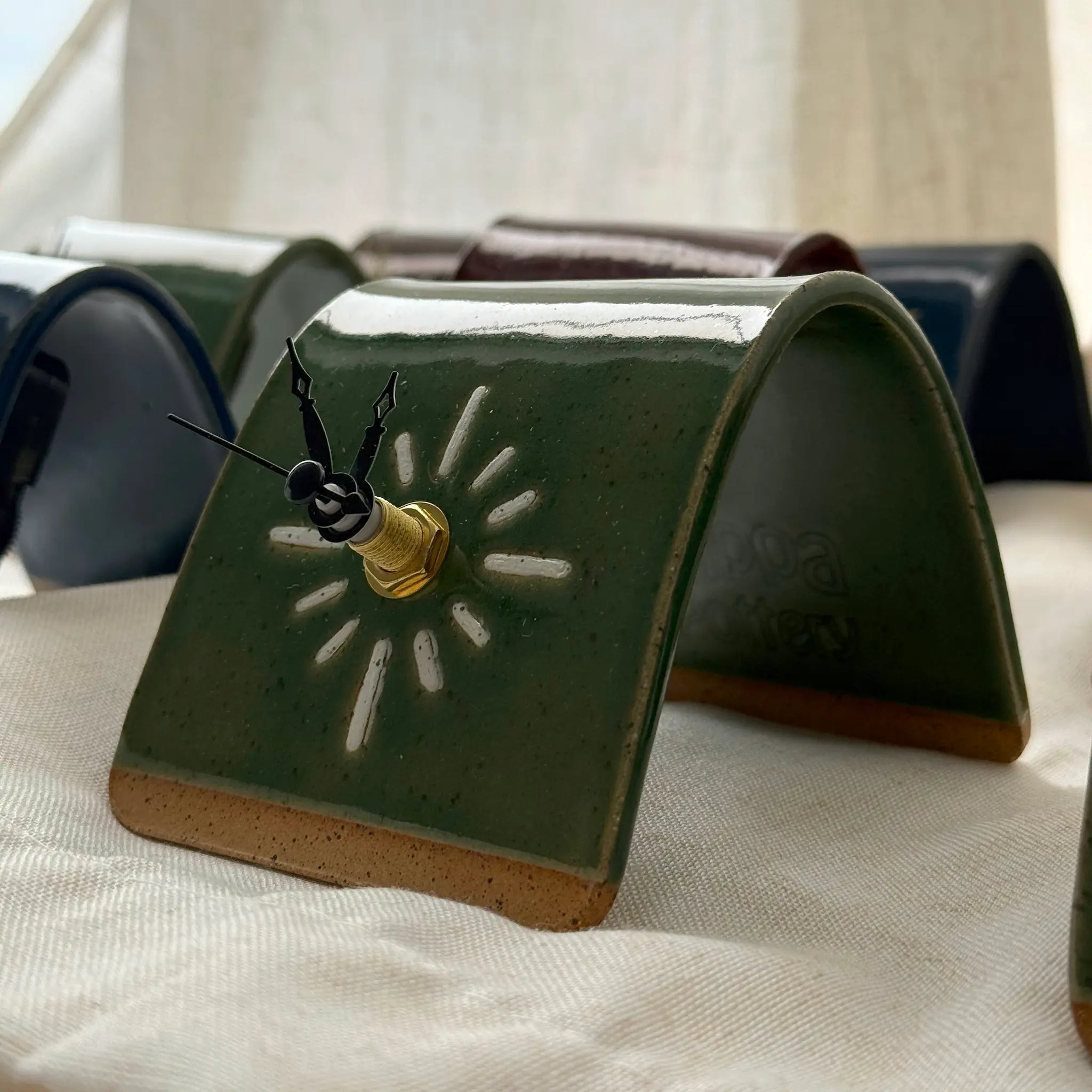 Green ceramic clock with sun design and black hands on a white textured surface.