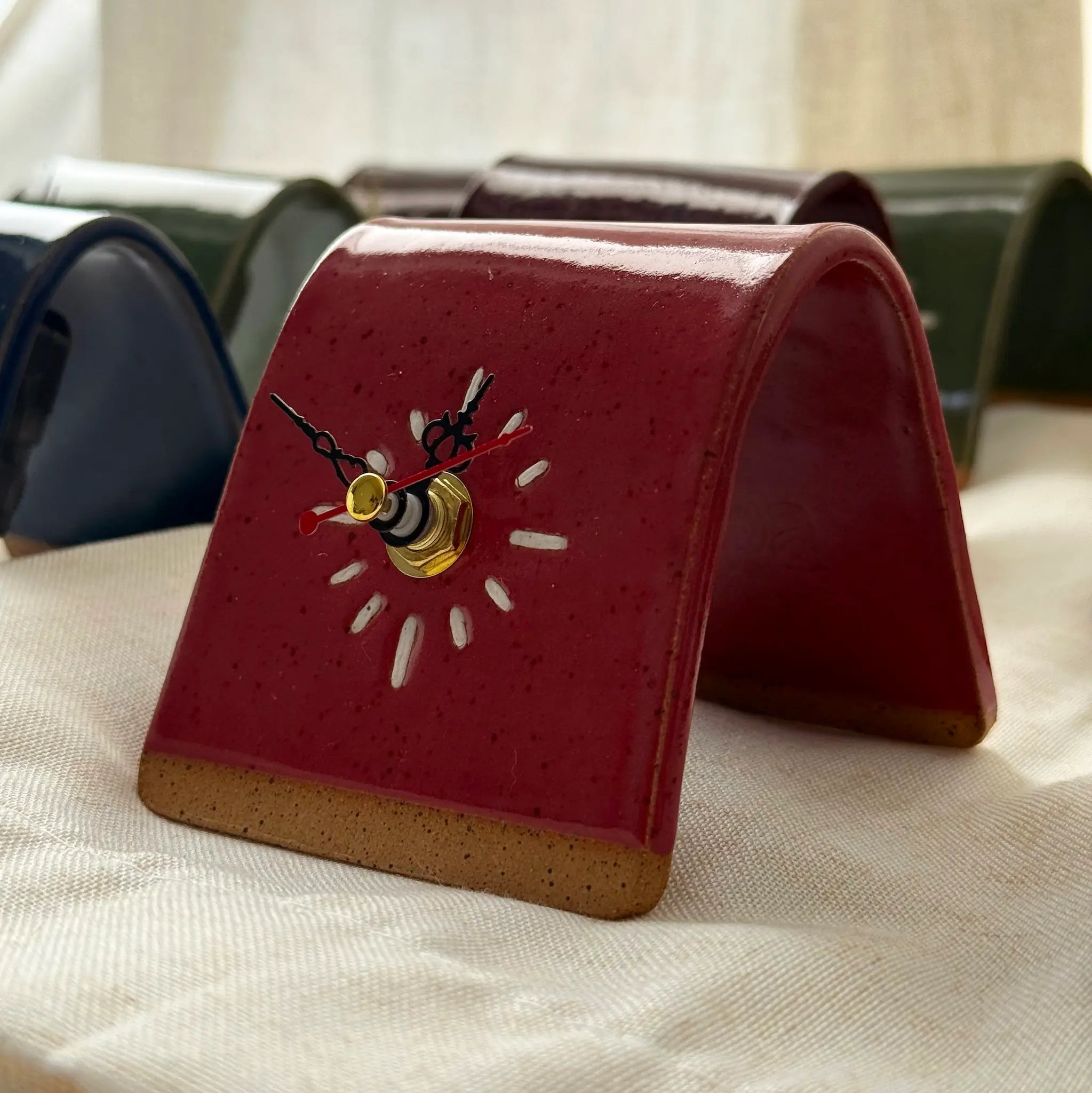 Red handmade ceramic clock with black and red hands on a beige textured surface.